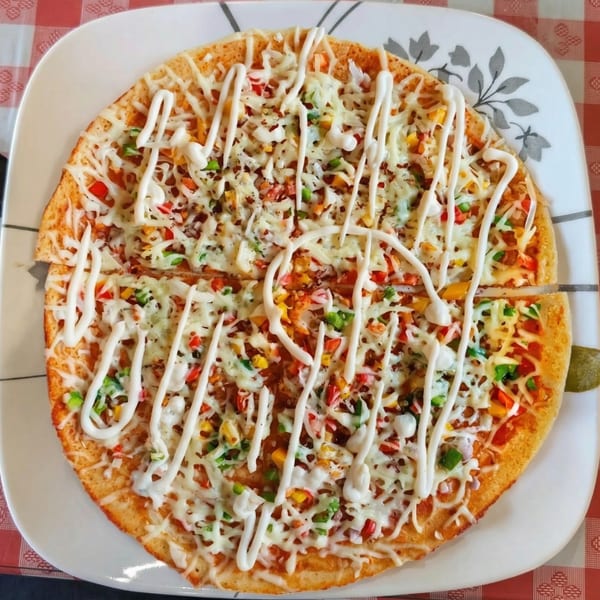 A round pizza with melted cheese, colorful vegetables, and white sauce drizzled on top.