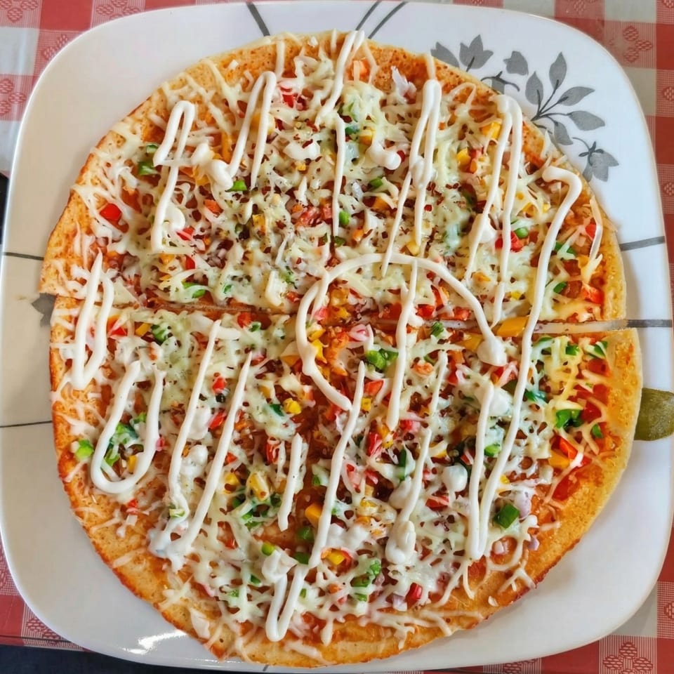 A round pizza with melted cheese, colorful vegetables, and white sauce drizzled on top.