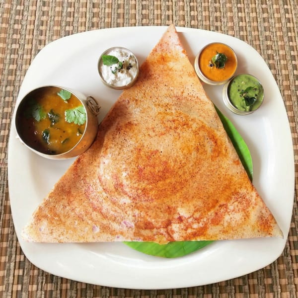 Crispy golden dosa, folded into a triangle, served with sambar and three chutneys on a white plate.